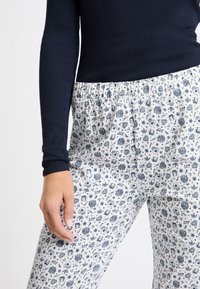 Marinblå ribbat långärmad topp som matchas med pyjamasbyxor med elastisk midja, med en vit bakgrund och blå grafiska mönster av presenter, hjärtan och blommor.