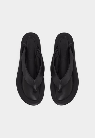 Pár černých polstrovaných žabek se širokými pásky a zaoblenými čtvercovými podrážkami, zobrazený zhora na bílém pozadí.