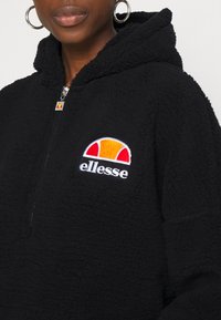 Sort fleece-pullover med hætte, der har en frontlynlås og et broderet elledese-logo i hvid, orange og rød på brystet.