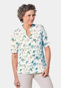 Blusa a maniche corte con un motivo floreale blu e grigio su uno sfondo chiaro, con scollatura a V e una texture di tessuto liscia.