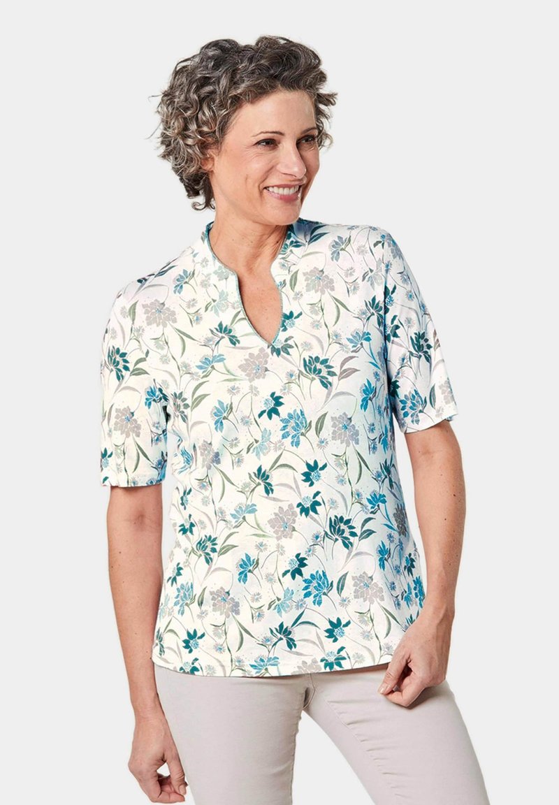 Blusa a maniche corte con un motivo floreale blu e grigio su uno sfondo chiaro, con scollatura a V e una texture di tessuto liscia.