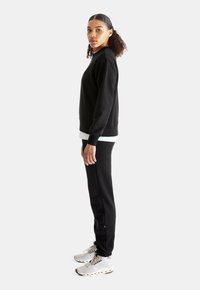 Black fleece sweatshirt and matching joggers worn with gray athletic shoes. Sweatshirt has a classic cut; pant legs taper at the ankle.