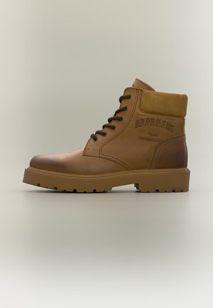 Bottine marron en cuir à lacets avec col rembourré et semelle texturée, portant la marque "Replay Blue Jeans" sur le panneau latéral.