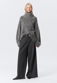 Pulover supradimensionat din mohair gri, cu guler înalt, asortat cu pantaloni largi de culoare gri închis și o curea neagră, având o cataramă argintie.