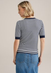 Top de punto de manga corta a rayas en azul marino y blanco, con cuello y dobladillo acanalados, combinado con una falda de mezclilla azul que cuenta con bolsillos traseros.