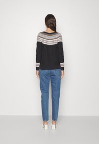 Svart tröja med ett geometriskt stickat mönster i vitt och brunt vid halsringningen, kombinerad med ljusblå jeans och vita klackskor.