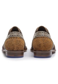 Chaussures en suede marron avec un capuchon de département texturé et un dessus à motifs. Talon légèrement surélevé avec un accent bleu. Vue arrière montrant les détails du design.