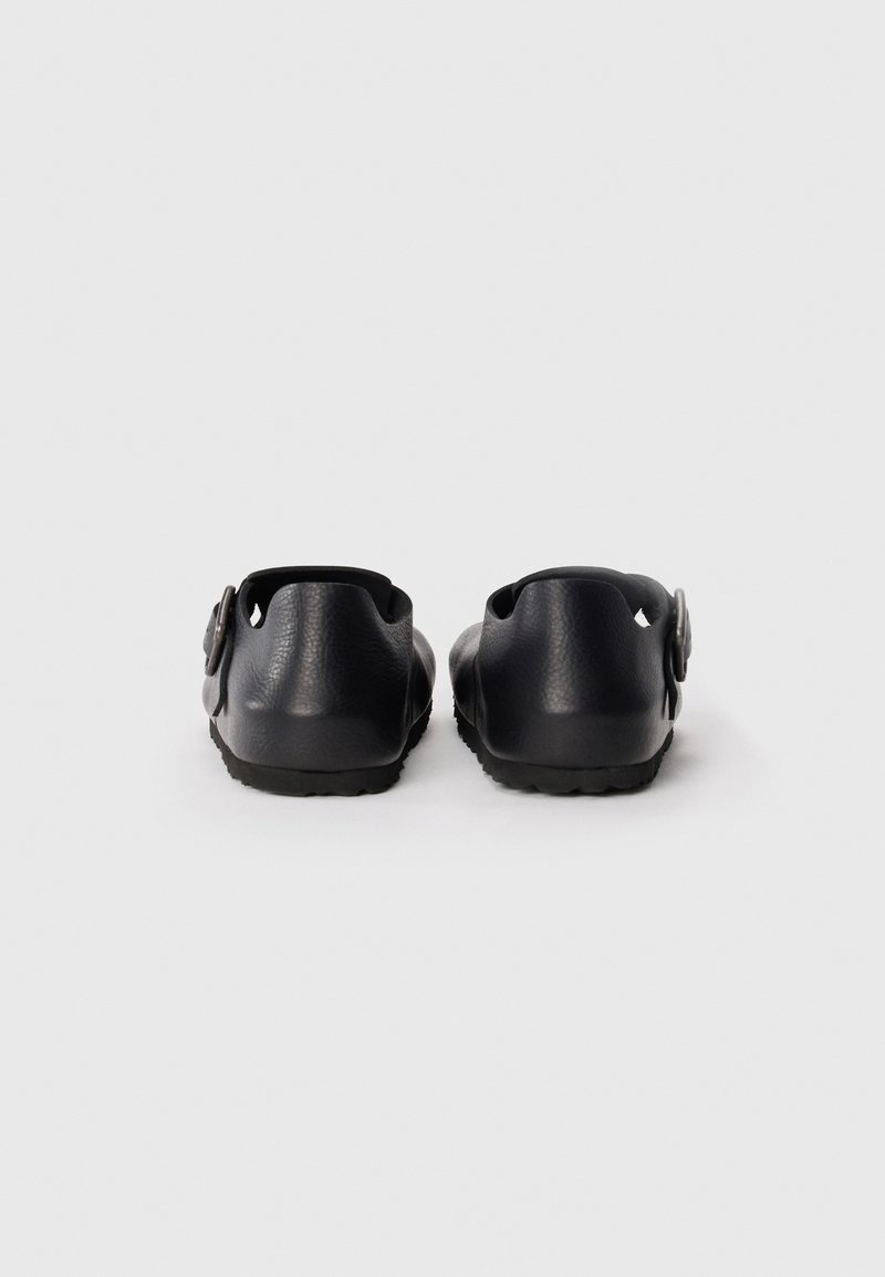 Black rubber clogs with a textured finish, open back, circular hardware accent, and a ridged sole for traction.