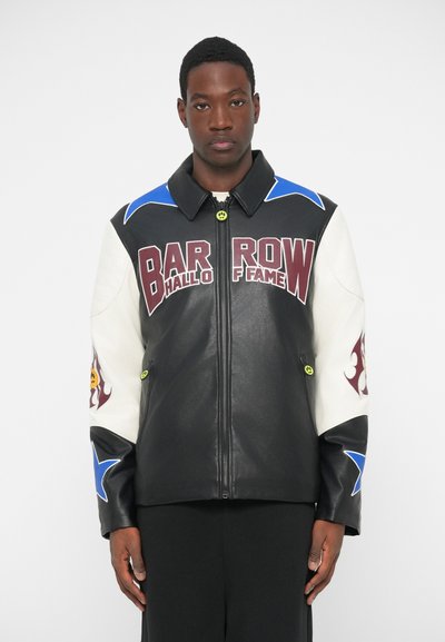 Schwarze Lederjacke mit weißen Ärmeln. Bietet kräftige weinrote Schriftzüge, blaue Sterne und einzigartige Muster. Reißverschluss vorne und gelbe Beschläge.