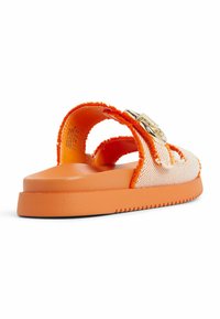 Sandal blanc et orange avec des sangles en tissu texturé et une boucle dorée. Dispose d'une semelle orange plate et large avec des bords crantés pour une meilleure adhérence.