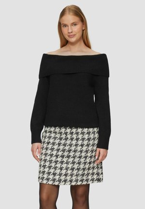 Maglione nero off-the-shoulder con scollatura a costine, abbinato a una gonna a tubo in tessuto houndstooth bianco e nero, che esalta un design pulito.