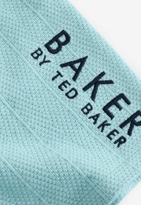 Svetle tyrkysové látce s texturovaným vzorem je vyšívaný nápis "BAKER BY TED BAKER" tmavě modrou barvou.