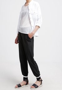 Vit skjorta med knappar, grå genomskinlig tanktop, svarta avsmalnande byxor med vita detaljer, svarta sandaletter med remmar och en texturerad sula.