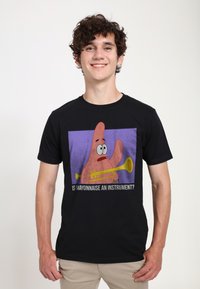Black cotton t-shirt featuring a cartoon character holding a yellow trumpet with a purple background and the text “IS MAYONNAISE AN INSTRUMENT?”