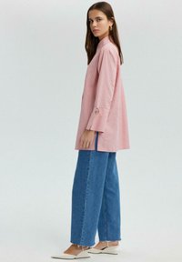 Chemise à rayures roses à manches longues avec une fente sur le côté, associée à un jean large bleu taille haute. Tissu doux, coupe décontractée et manches à revers.