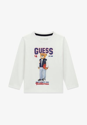Chemise blanche à manches longues avec un ours en peluche portant une veste universitaire tenant un ballon de basket, texte "GUESS LA EST. 1981 California" sur le devant.