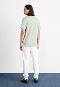 T-shirt de algodão verde-claro com mangas curtas, combinado com sweatpants brancos e ténis pretos. Design simples e descontraído, sem embelezamentos.