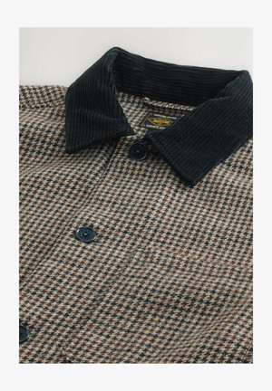 Veste à carreaux marron et noir avec un col en velours côtelé, fermeture à boutons et tissu texturé. Motif et contraste de couleurs notables.