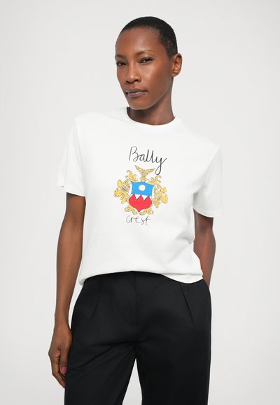 White short-sleeve t-shirt featuring a colorful graphic design with a crest, "Bally" text, and intricate gold accents. Black pants.