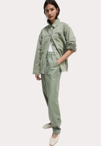 Lichtgroene, oversized jas en bijpassende broek van zachte stof. Witte top eronder. Witte instappers maken de look compleet.