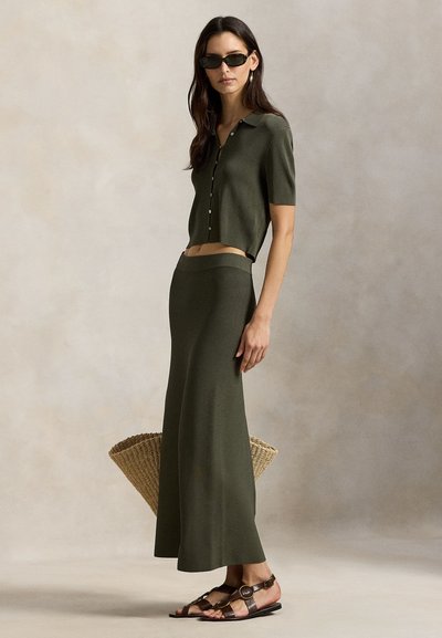 Ελιά πράσινο cropped πλεκτό τοπ με κουμπιά και ταιριαστό μακρύ φούστα. Πλεκτή ψάθινη τσάντα και καφέ σανδάλια με λουράκια ολοκληρώνουν την εμφάνιση.