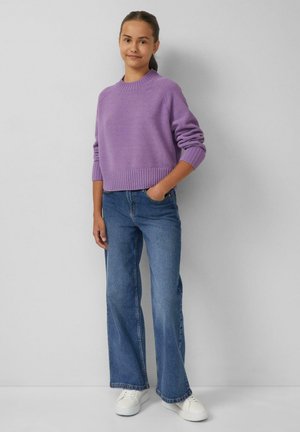 Paarse cropped trui met geribbelde onderrand, gecombineerd met blauwe wijde jeans en witte sneakers. Achtergrond is lichtgrijs.