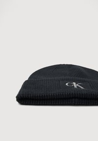 Μαύρο πλεκτό καπέλο με ριγωτή υφή, διαθέτοντας διπλωμένο τελείωμα και ραμμένο λογότυπο σε ασημί.