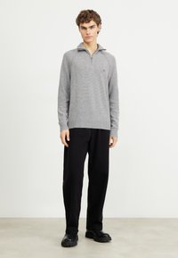 Pull en maille gris avec un col zippé demi-long, des poignets et un ourlet côtelés. Associé à un pantalon noir ample et des chaussures noires chunky.