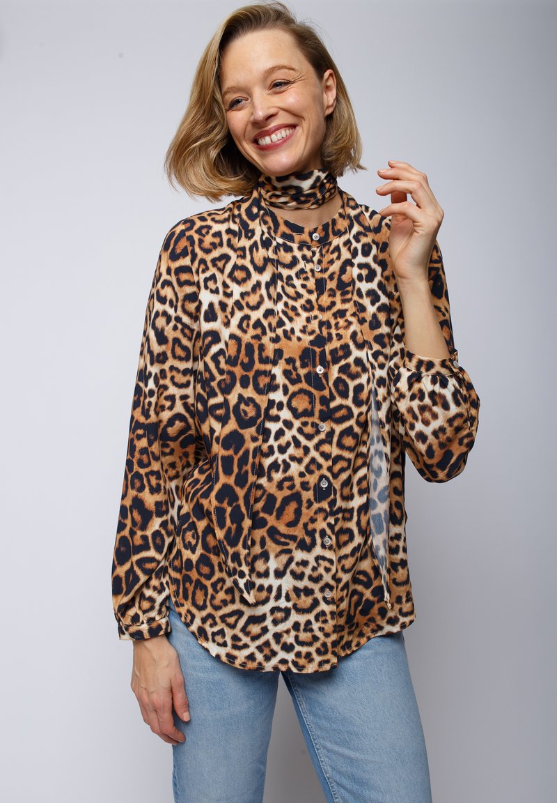 Bluzka w panterkę w odcieniach brązu i czerni, z długimi rękawami, zapinana na guziki i z wysokim kołnierzem. Miękki materiał o gładkiej fakturze.