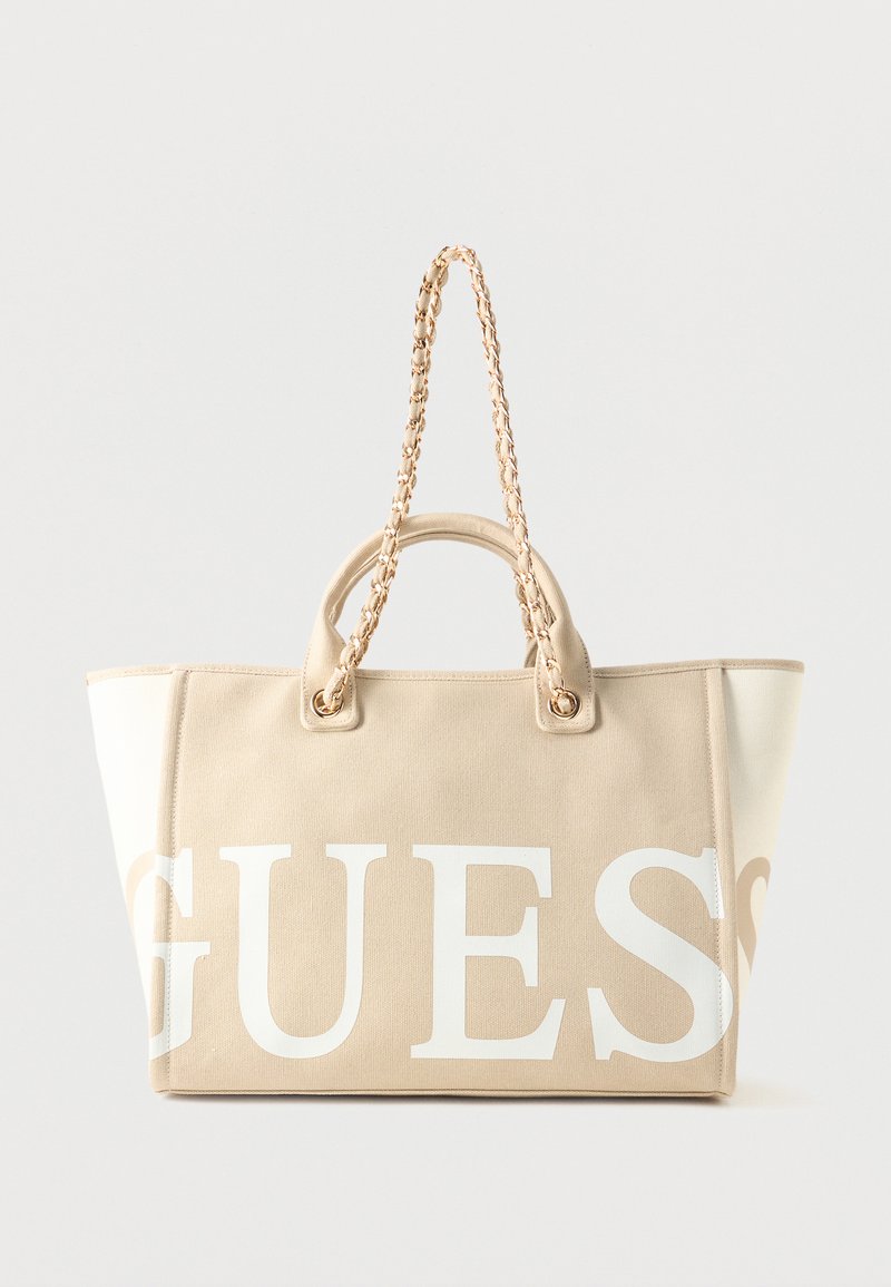 Sac cabas en toile beige et blanche avec logo « GUESS » en grandes lettres blanches et anses tressées avec détails en chaîne dorée.