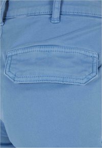 Gros plan d'une poche en tissu bleu clair sur un vêtement avec des coutures détaillées et une passants de ceinture au-dessus de la poche.