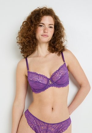 Sotto intimo in pizzo viola con slip coordinato, caratterizzato da bordi smerlati, motivi floreali e spalline regolabili con elementi decorativi.