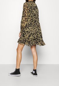 Abito floreale nero con maniche lunghe, orlo smerlato e motivo a fiori multicolore, abbinato a sneakers alte nere.