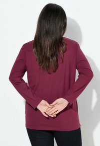 Bordeaux lange mouw shirt met een ontspannen pasvorm, ronde halslijn en een zachte textuur, gecombineerd met donkere jeans. Eenvoudig achteraanzicht.