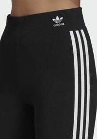 Černé sportovní legíny s vysokým pasem, na bocích se třemi bílými svislými pruhy a malým bílým logem na vrchu.