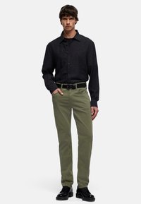 Camicia nera con bottoni, pantaloni verde oliva, cintura nera e scarpe nere. La camicia ha un colletto classico e maniche lunghe; i pantaloni sono a gamba dritta.
