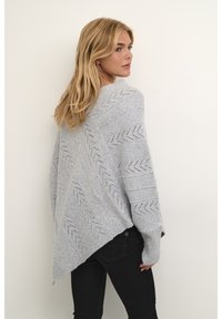 Gaišpelēka adīta pončo ar zigzaga rakstu, platām piedurknēm un diagonālu apakšmalu, ar teksturētu apdari un brīvu piegriezumu.