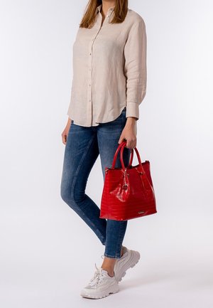 Borsa tote in finta pelle rossa con texture effetto coccodrillo e doppi manici, dotata di chiusura a cerniera e dettagli metallici. Abbinata a jeans e sneakers.