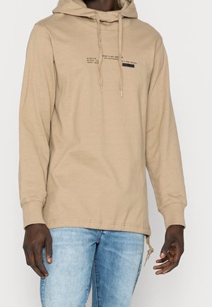 Sudadera de manga larga en color beige claro con cordones ajustables, detalle de texto en el frente y un corte relajado. Tejido de algodón suave y liso.