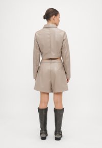 Beige faux leather cropped jacket paired with matching high-waisted shorts, featuring a belt and back pleats. Styled with gray knee-high boots.
