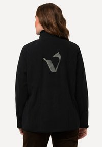 Černá bunda s vysokým límcem a velkým šedým logem na zadní straně. Materiál vypadá jemně s texturovaným povrchem.