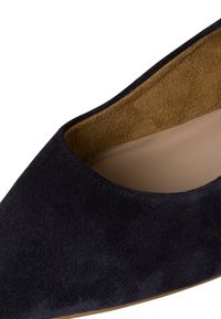 Zapato de tacón alto de ante azul marino con punta afilada y un forro interior suave en color beige. Presenta una textura suave y un diseño minimalista.