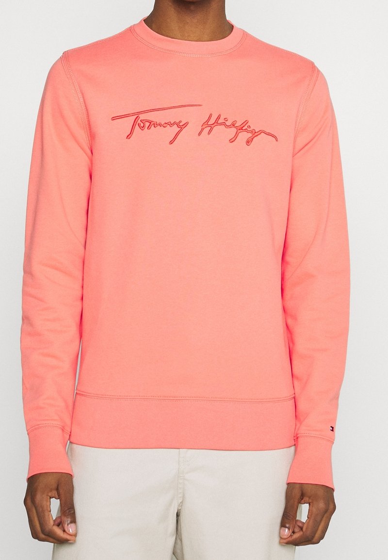 Sweat-shirt corail à manches longues, col rond, avec logo "Tommy Hilfiger" brodé. Caractérisé par une texture lisse et des poignets côtelés.