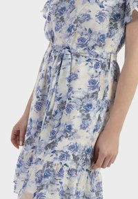 Lange jurk van een lichtgewicht stof met blauwe, grijze en gele rozenpatronen, met een gestrikt taille en ruches aan de onderkant.
