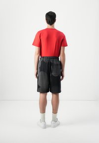 T-shirt rossa a maniche corte con un taglio semplice, abbinata a pantaloni corti neri con grandi motivi astratti grigi. Sneakers bianche e calzini leggeri.