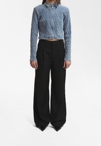Giacca in denim trapuntato blu chiaro con zip frontale, abbinata a pantaloni larghi neri a vita alta e tacchi a punta neri.
