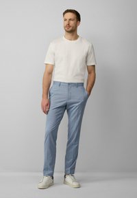 Helleblau gestreifte Hose mit flacher Vorderseite und Seitentaschen, kombiniert mit einem schlichten weißen T-Shirt mit Rundhalsausschnitt und weißen Sneakers.