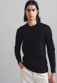 Melna garām piedurknēm t-kreklā ar pieguļošu dizainu, izgatavots no gludas auduma. Apaļais kakla izgriezums bez redzamām detaļām vai rakstiem. Valkāts ar gaišiem biksēm.