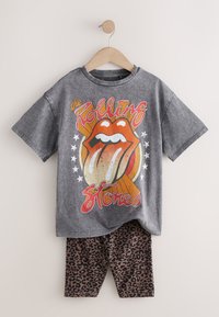 Szürke pamut póló, amely egy színes Rolling Stones grafikát ábrázol, valamint egy pár barna leopárdmintás leggings, fa vállfán függve.