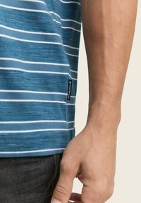 Camisa de manga corta a rayas en azul y blanco, con un tejido texturizado, dobladillo recto y una etiqueta de marca negra en el lado.
